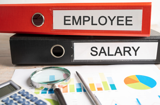 binders titled Employee and Salary with calculator, magnifying glass and pen on top of a paper with charts and graphs